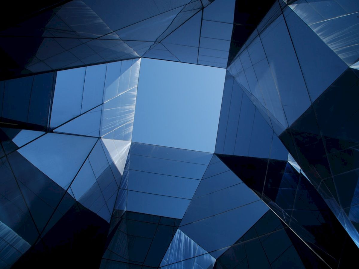 Geometric architecture with reflective surfaces forms a square opening to the sky, showcasing modern design and lighting.
