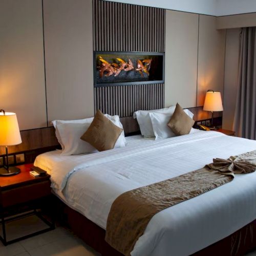 A cozy hotel room with a king-sized bed, bedside lamps, and a decorative wall feature, exuding a warm, inviting ambiance.