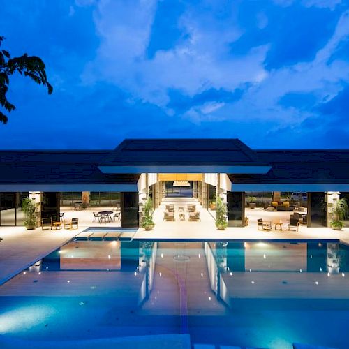 A luxurious outdoor pool area at night, with a modern building illuminated in the background and a clear sky overhead.