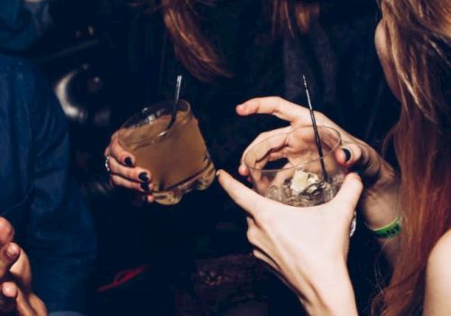 People are laughing and holding drinks at a social gathering or party, with visible straws and glasses in hand.