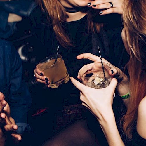 People are laughing and holding drinks at a social gathering or party, with visible straws and glasses in hand.
