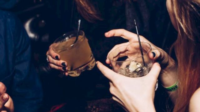 People are laughing and holding drinks at a social gathering or party, with visible straws and glasses in hand.