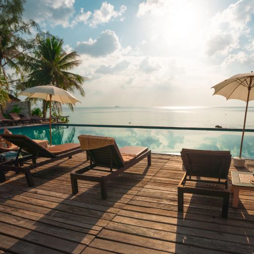 Poolside view with lounge chairs and umbrellas, overlooking a serene ocean under a bright sky with scattered clouds.