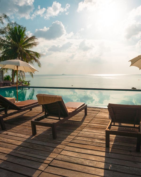 Poolside view with lounge chairs and umbrellas, overlooking a serene ocean under a bright sky with scattered clouds.