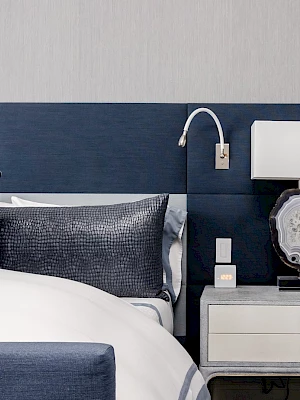 A modern bedroom with a navy blue headboard, pillows, a side table, and a lamp featuring a decorative stone base.