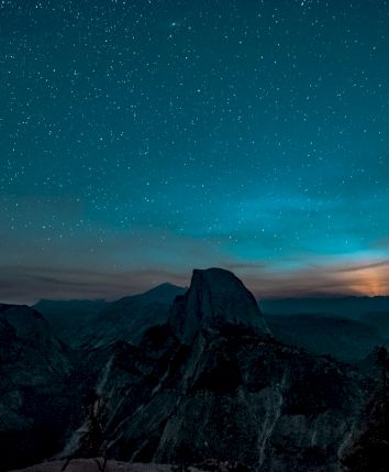 A starry night sky over a mountainous landscape with a glowing horizon.