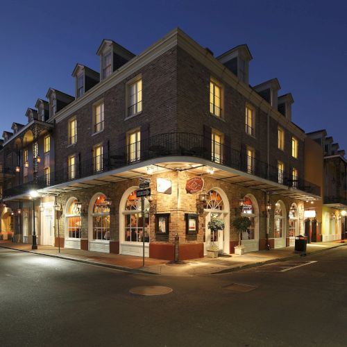 A brightly lit corner building at dusk with balconies and arched windows, situated in an empty, quiet street.