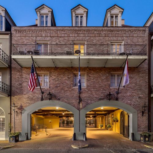 The image depicts a building with brick facade, balconies, and two flags with arched entryways.