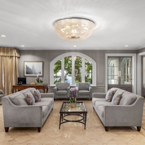 A luxurious living room with a chandelier, elegant furniture, and a fireplace, featuring large windows and tasteful decor.