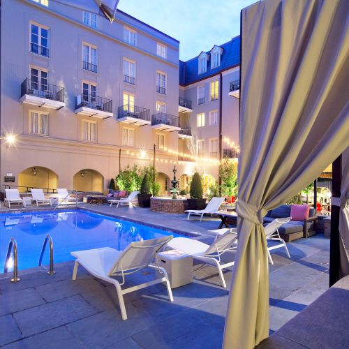 The image shows a luxurious outdoor pool area with lounge chairs, a cabana, and ambient lighting in a building's courtyard setting.