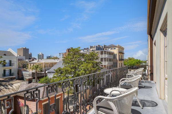 A rooftop view of a city scene with a metal-railed balcony, white chairs, historic buildings, and a clear blue sky.