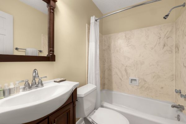 A clean bathroom with a sink, mirror, toilet, and bathtub. There are toiletries on the sink and a towel on a rack.