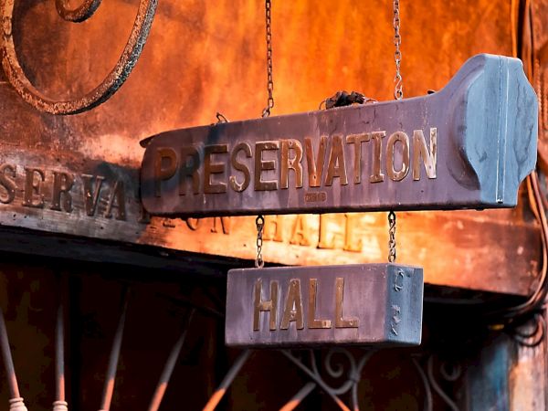 A weathered wooden sign reads "Preservation Hall" hanging above an entrance with warm, rustic tones and metalwork decor.