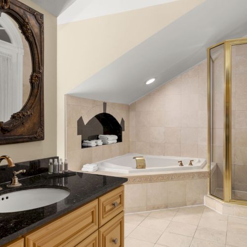 Luxurious bathroom with a granite countertop, ornate mirror, corner bathtub, glass shower, and elegant fixtures.