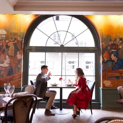 A couple dining in a restaurant with large windows and vibrant wall murals, sitting across from each other enjoying their meal.