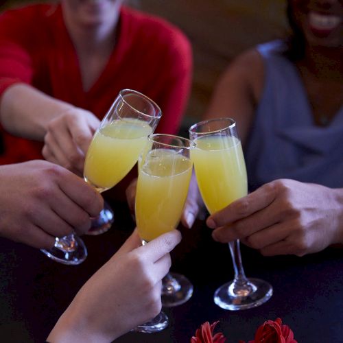 People are toasting with glasses of yellow drinks, possibly mimosas, in a celebratory setting.
