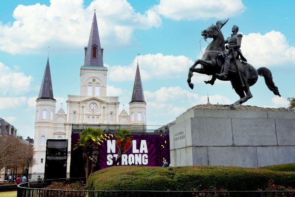 A church with three spires, a statue of a rider on a horse, and a "NOLA STRONG" sign are in the image.