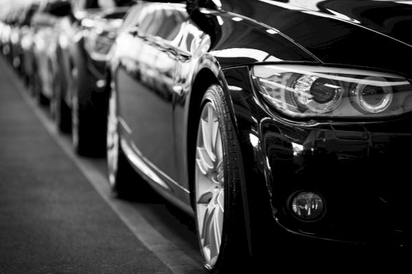 A close-up of parked cars in a row, with a focus on a sleek black vehicle's front and headlights.