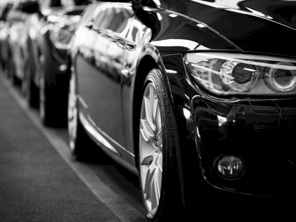 A close-up of parked cars in a row, with a focus on a sleek black vehicle's front and headlights.
