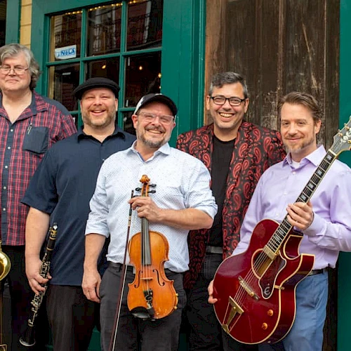 A five-member band posing outside a vintage-style storefront: saxophonist, violinist, guitarist, and two other musicians smiling with instruments, ready to play.