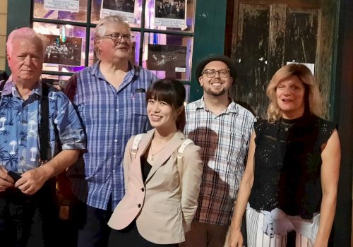 A group of five adults posing together outside a storefront at night, smiling for the camera.
