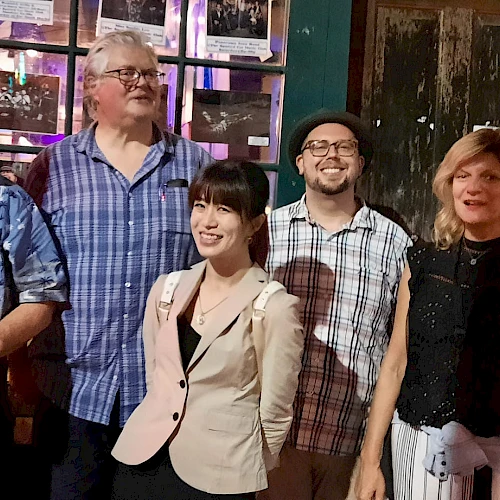 A group of five adults posing together outside a storefront at night, smiling for the camera.