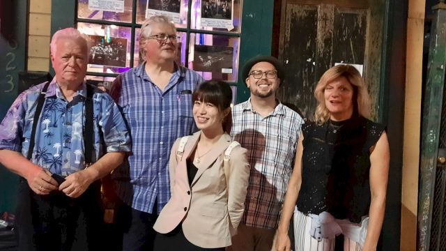 A group of five adults posing together outside a storefront at night, smiling for the camera.