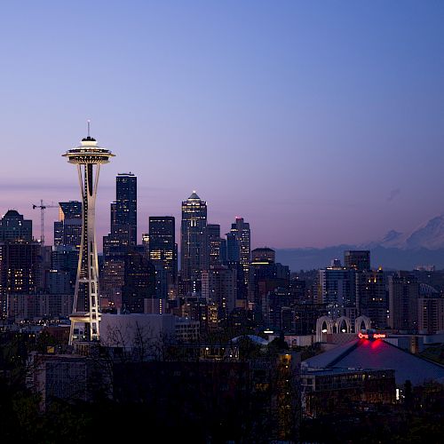 A cityscape featuring the Space Needle, Seattle skyline, and Mount Rainier in the background during dusk under a clear sky.